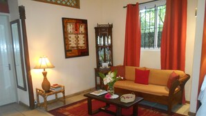 Uma sala de estar com sofá, mesa de centro, luminária, relógio na parede e janela com cortinas.