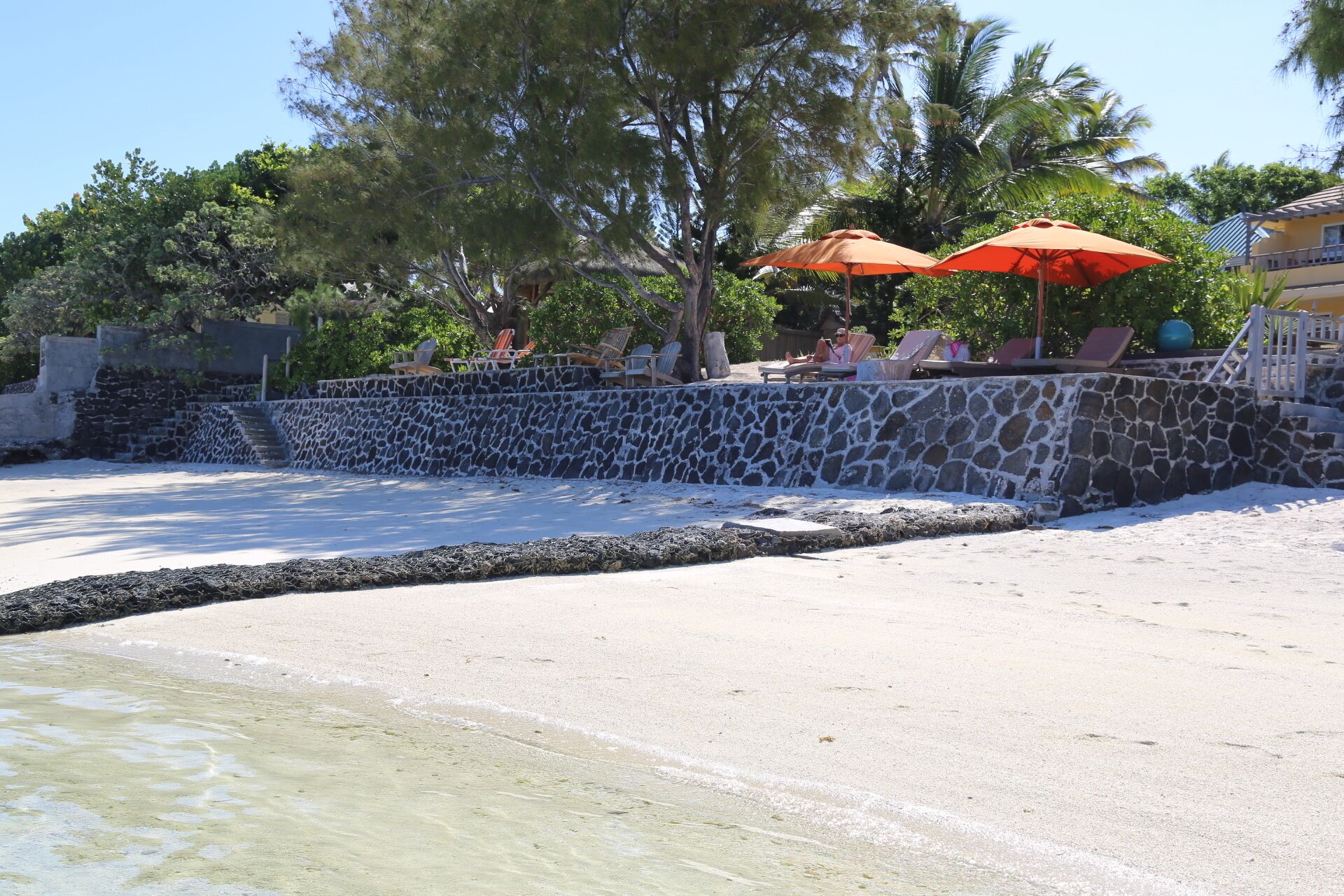 A beach with a stone wall, lounge chairs, and orange umbrellas.