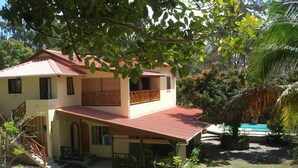 Uma casa de dois andares com varanda, escada e piscina ao fundo.