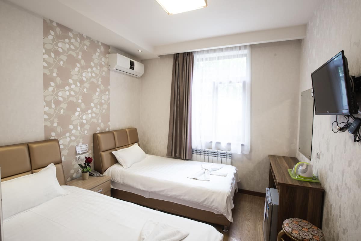 A hotel room with two beds, a TV, a desk, and a window with curtains.