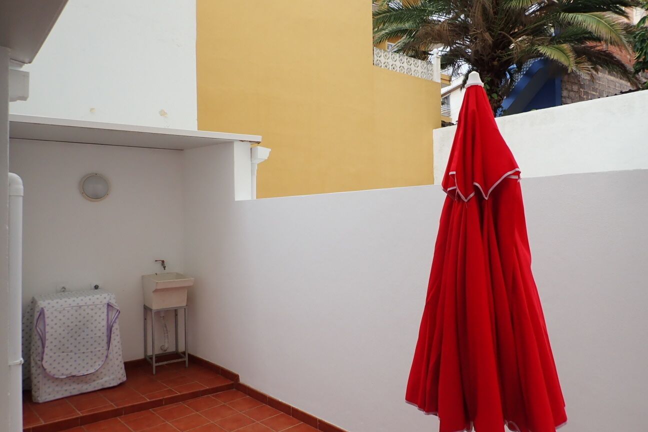 Een klein, afgesloten buitengebied met een witte wasbak, een klein wit kastje en een rode parasol.