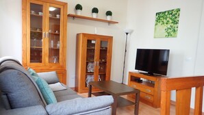 Una sala de estar con un sofá gris, armarios de madera, un televisor y una lámpara de pie.
