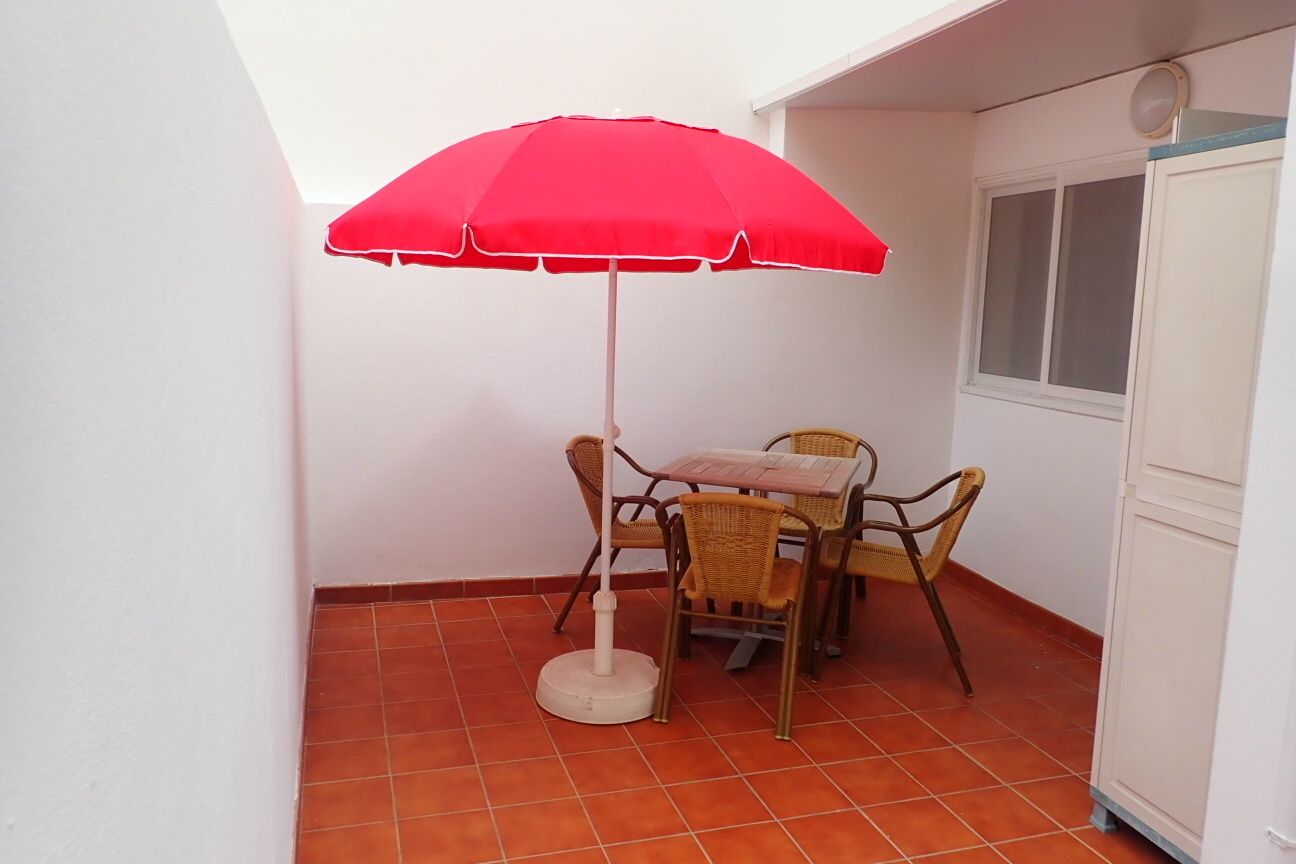 A small patio area with a red umbrella, wicker chairs, and a tiled floor.