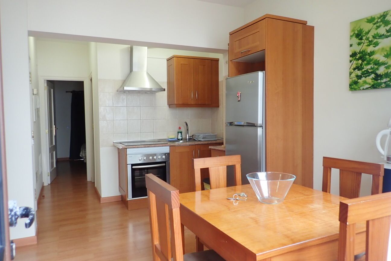 A compact kitchen with wooden cabinets, a stainless steel refrigerator, and a dining table with chairs.