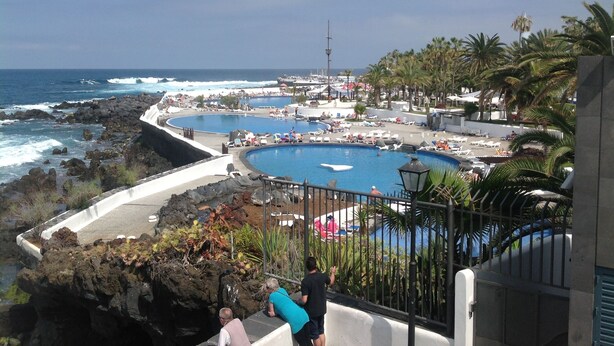 Un complejo turístico frente al mar con varias piscinas, una costa rocosa y palmeras.