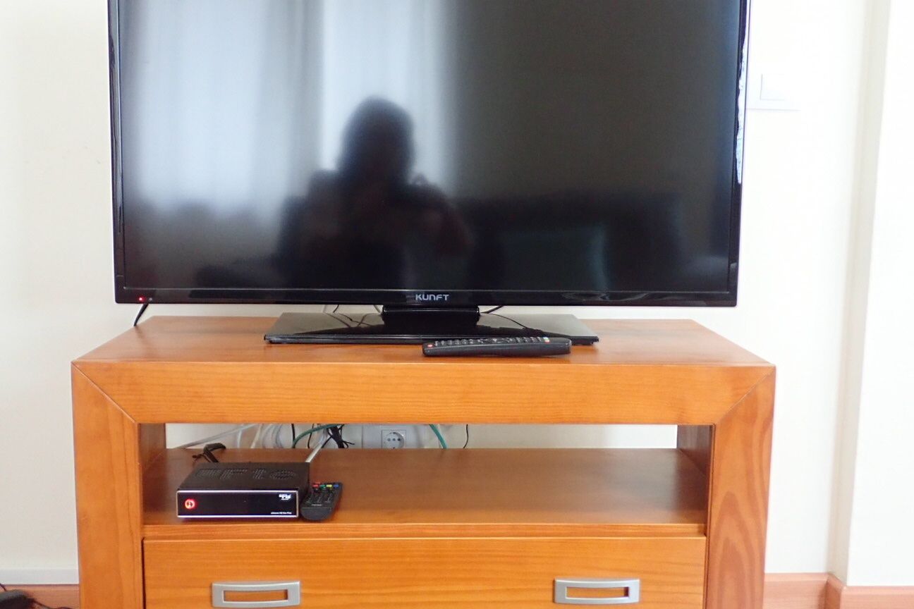 A television on a wooden stand with a remote control and a cable box.