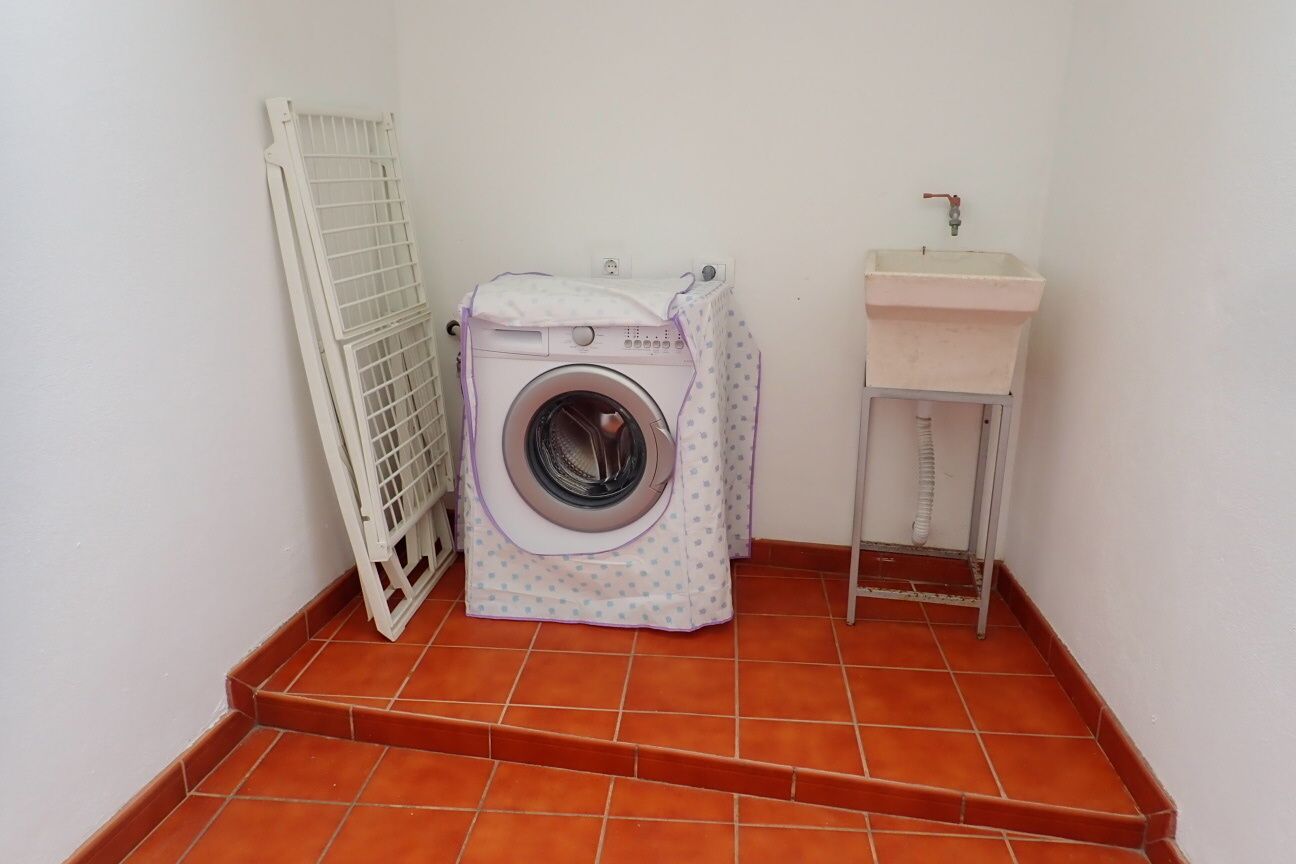 A compact laundry area with a washing machine, a drying rack, and a sink.