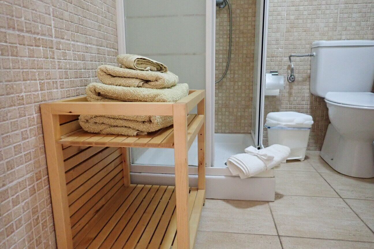 A bathroom with a wooden shelf holding towels, a shower area, and a toilet.