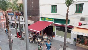 Una plaza con mesas al aire libre, palmeras y comercios, incluyendo 'Ca Mario' y 'Ceylon'.