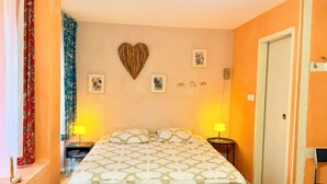 Een slaapkamer met een bed, twee bedlampen, een hartvormige decoratie en foto's in lijsten aan de muur.