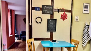 Een kamer met een blauwe tafel, twee houten stoelen, een schoolbord met teksten, een nummerbord en een wanddecoratie.