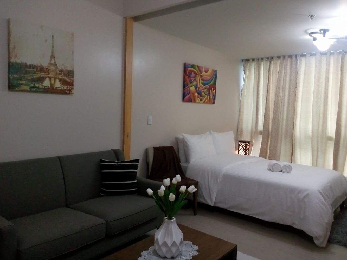 A hotel room with a bed, a sofa, a small table with a vase of flowers, and two paintings on the walls.