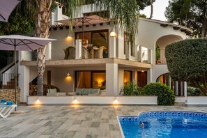 Una casa de dos pisos con piscina, mobiliario exterior y una escalera.