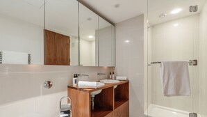 Ein modernes Badezimmer mit Waschtisch aus Holz, zwei Waschbecken, einem großen Spiegel und einer Duschkabine.