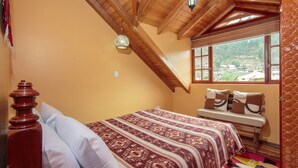 Un dormitorio con techo de madera, una cama con ropa de cama estampada, un banco con cojines y una ventana con vistas a la vegetación.