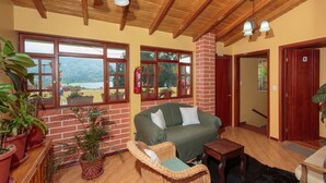 Una habitación acogedora con techo de madera, un sofá verde, un sillón de mimbre y plantas en macetas.