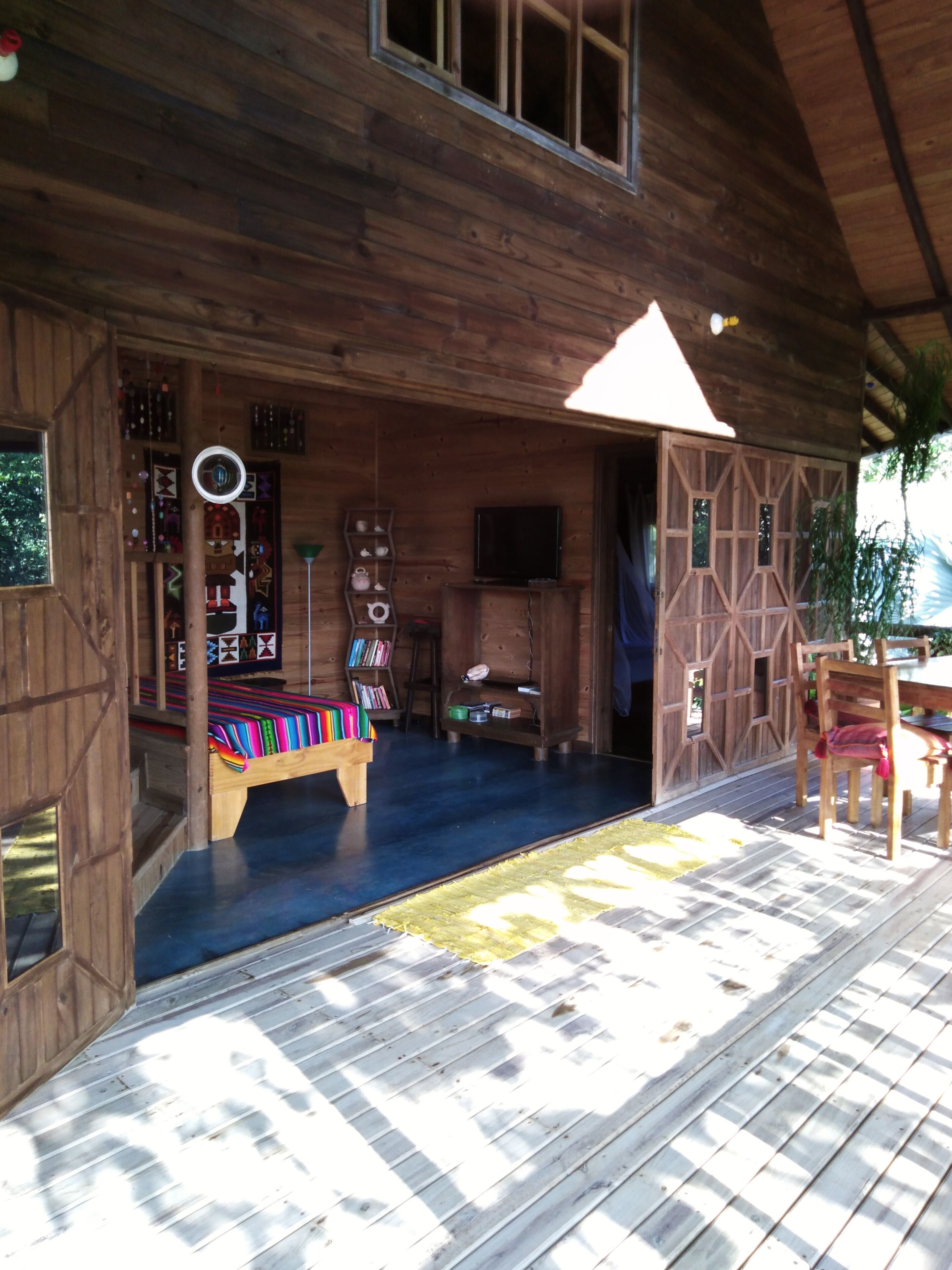 A wooden cabin interior with a bed, shelves with books, a television, and a dining area.
