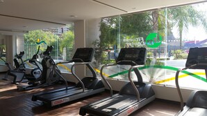 A gym with treadmills and stationary bikes, large windows with a view of the street and greenery. - Bahia Escondida, excelentes vacaciones en un paraiso!! (Santiago)
