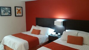 A hotel room with two beds, each with white bedding and orange accents. There is a nightstand with a lamp and a phone between the beds. The room has a red accent wall and two framed artworks above the beds. - Bahia Escondida, excelentes vacaciones en un paraiso!! (Santiago)
