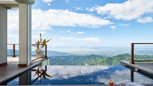 Una terraza de madera con piso de vidrio, con vista a un paisaje urbano y montañas.