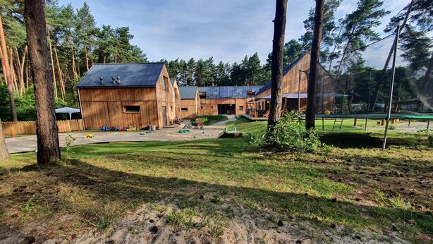 A rustic wooden building with a metal roof, surrounded by a grassy yard and tall trees.
