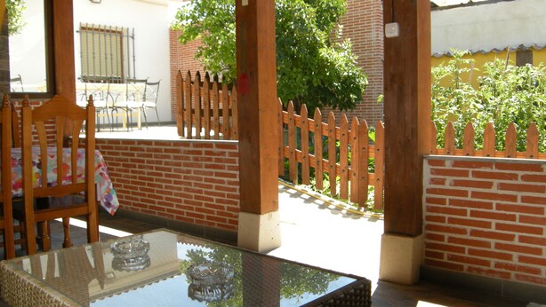 A covered patio with a glass-top table, wicker chairs, and a wooden fence.