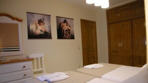 A hotel room with two beds, a wooden wardrobe, a white dresser, and two paintings on the wall.