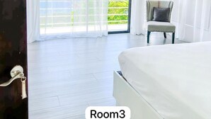Un dormitorio con una cama grande, una silla y un ventanal corredera que da a un balcón con vistas a zonas verdes.