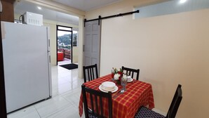 Ein Essbereich mit einem Tisch für zwei Personen, einem Kühlschrank und einer Tür, die auf einen Balkon mit Hügelblick führt.
