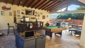 Eine Außenbar mit Billardtisch, Barhocker und Pool.