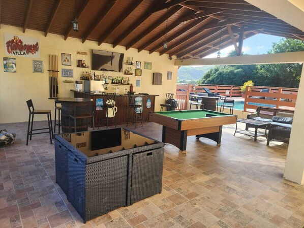 Un área de bar al aire libre con mesa de billar, taburetes de bar y piscina.