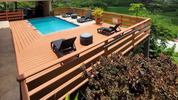 Eine Holzterrasse mit Swimmingpool, Liegestühlen und Blick auf eine grüne Landschaft mit Hügeln.