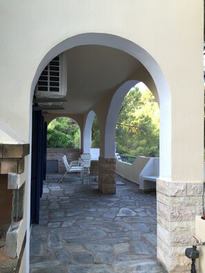A covered outdoor patio with stone flooring, white chairs, and a view of greenery. - Modern villa in Kanapitsa, Skiathos  (Kanapitsa, Skiathos)