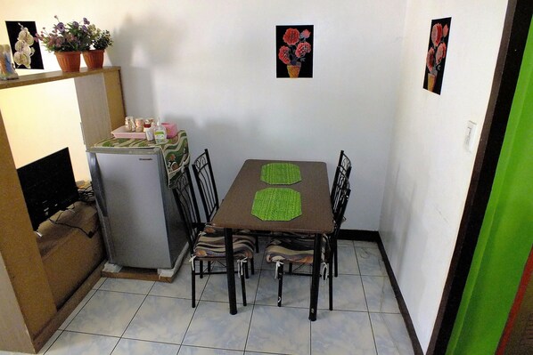 Una cocina compacta con refrigerador, una mesa de comedor con sillas y un estante pequeño con plantas en macetas.