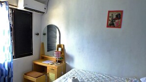 Una habitación con cama, escritorio, silla, espejo y un pequeño taburete.