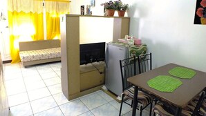 Un espacio habitable compacto con sofá, una mesa de comedor con sillas, un refrigerador y una pequeña zona de cocina.