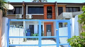 Una entrada con reja, unidades de aire acondicionado y un edificio con fachada marrón y naranja.
