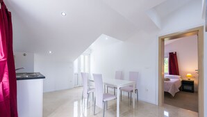 Une pièce moderne et bien éclairée, comprenant un coin repas, une kitchenette et une chambre avec un lit et une table de chevet.