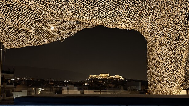 Une vue nocturne d’une ville, avec un bâtiment imposant illuminé sur une colline, entouré d’une structure décorative.
