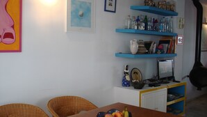 A dining area with wicker chairs, a wooden table with a fruit bowl, blue shelves with decorative items, and a black stove. - House of the rose. An explosion of color and beauty in a still virgin landscape. (Nijar)