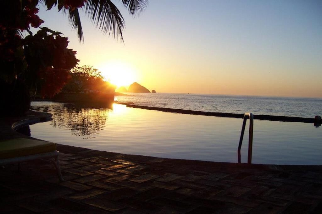 Une vue sur le coucher de soleil depuis une piscine à débordement, avec un palmier et une chaise.