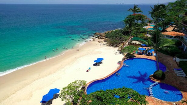 Un complejo turístico en la playa con piscina, acceso a la playa y vistas al océano.