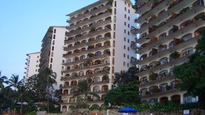 Un hotel de varios pisos con balcones en cada planta, rodeado de vegetación y palmeras.
