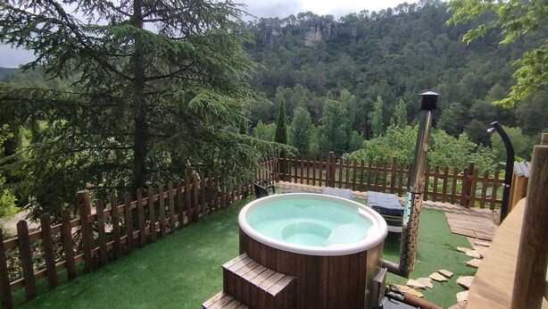 Een hottub omringd door een houten omheining, met uitzicht op een bebost helling.