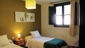 Een slaapkamer met twee bedden, een nachtkastje, een wandlamp, een raam met gordijnen en een radiator.