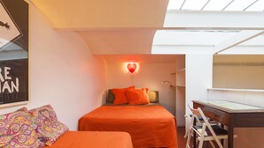A bedroom with two beds, a desk, and a skylight.