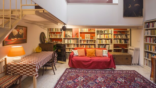 A cozy reading nook with a red sofa, a patterned rug, and a bookshelf filled with books.