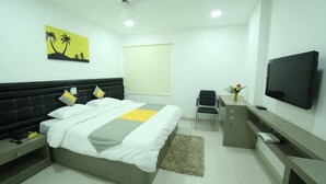 A modern hotel room with a bed, bedside table, TV, desk, chair, and a window. - Lariviera falcon nest in Madhapur  (Hyderabad)