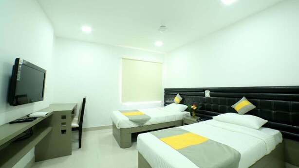A hotel room with two beds, a desk, a chair, a television, and a window. - Lariviera falcon nest in Madhapur  (Hyderabad)
