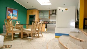 Un comedor con una mesa y sillas, una cocina con armarios y un refrigerador, y un cuadro en la pared.
